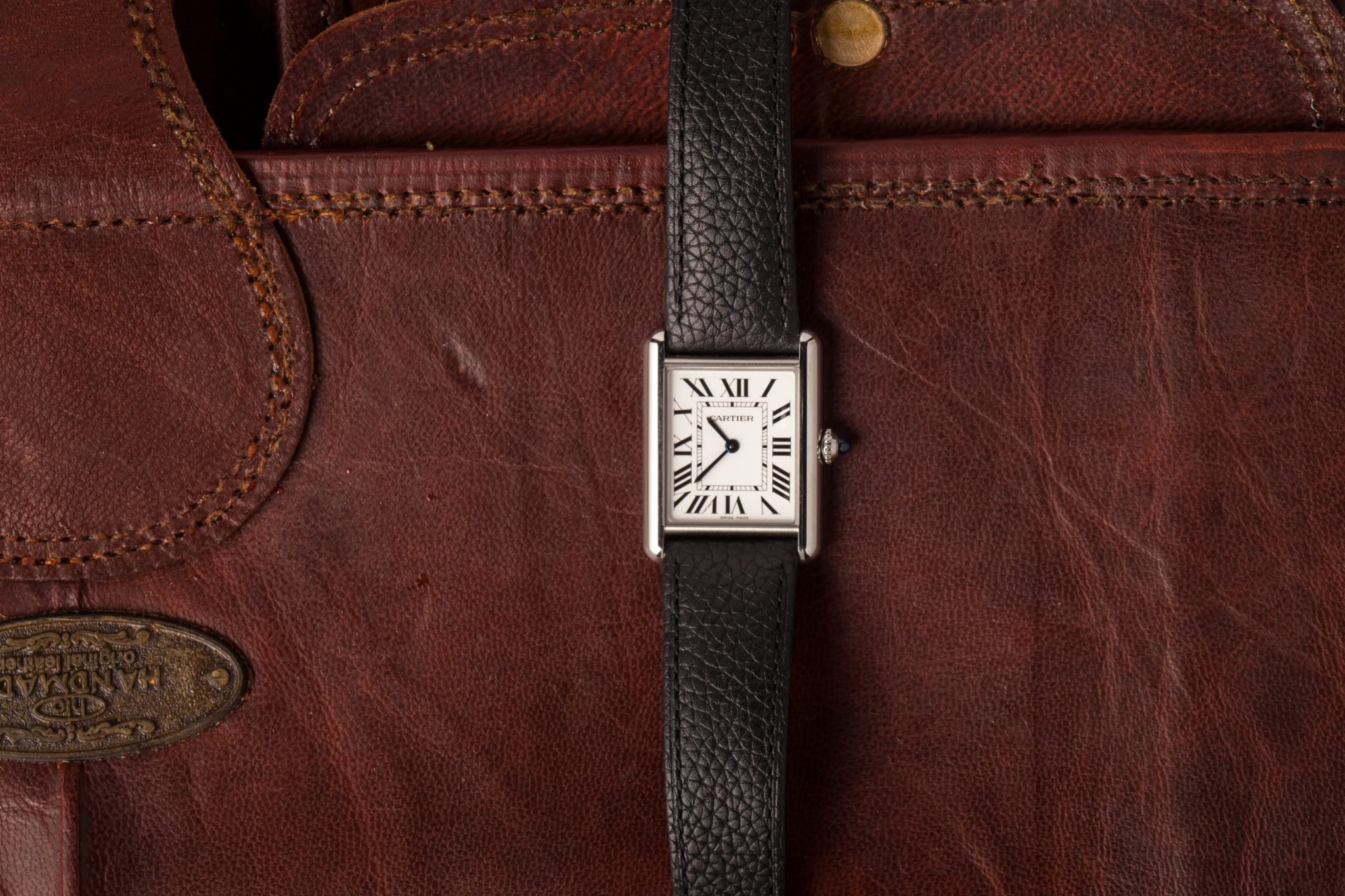 Cartier Tank watch with white square dial and black leather strap on a burgundy leather background