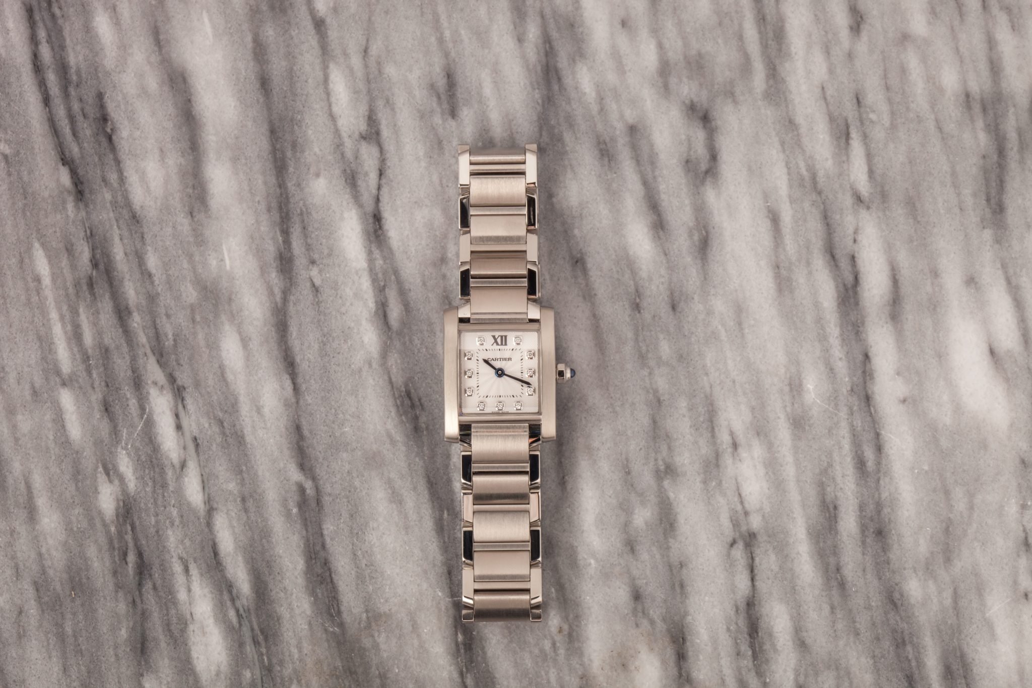 Cartier Tank watch with white rectangular dial and silver bracelet on a gray marble background